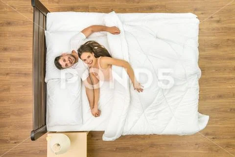 The happy couple look to the camera on the bed. View from above Stock Photos