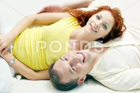 Happy couple lying on bed together and looking at camera Stock Photos