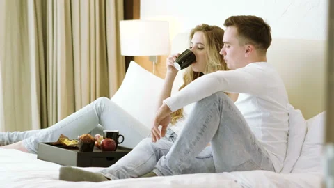 Happy couple lying in the bed. Young man, woman eating breakfast at bedroom. 4K 스톡 동영상 105670962