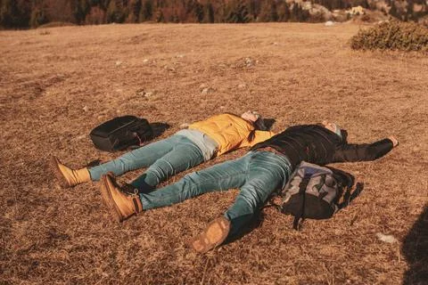 A happy couple lying on a meadow while resting on top of a mountain Stock Photos