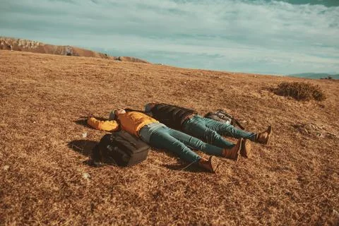A happy couple lying on a meadow while resting on top of a mountain Stock Photos