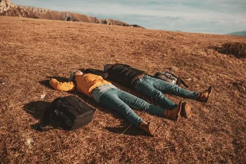A happy couple lying on a meadow while resting on top of a mountain Stock Photos
