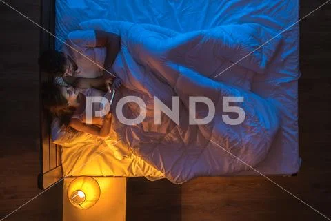 The happy couple with a phone lay on a bed. Evening night time. View from abo Stock Photos