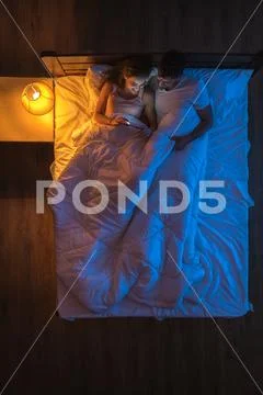 The happy couple with a phone lay on a bed. Evening night time. View from abo Stock Photos