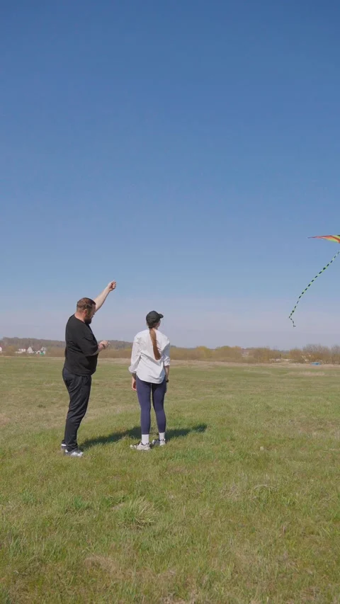 Happy couple playing and flying a kite in a green field Видео 344595928