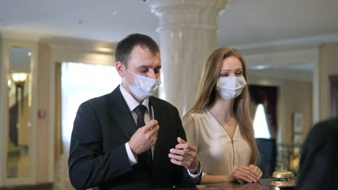 Happy couple in protective masks checking in at a hotel during a pandemic Stock Footage 141477282