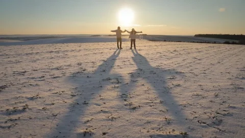 Happy couple raises joined hands in snowy meadow against clear sunset sky Stock Footage 328134841