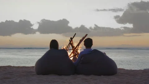 Happy couple resting in front of burning yellow campfire at evening on the Stock Footage 190551417