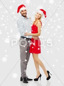 Happy couple in santa hats hugging over snow Stock Photos