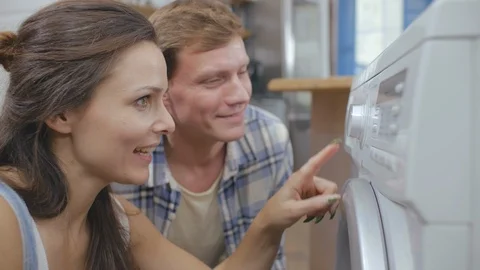 Happy couple setting program of washing machine doing laundry together Video stock 124844501