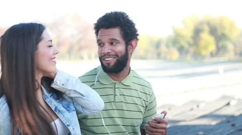 Happy couple with shared earphones listening to music at park Stock Footage 59555083