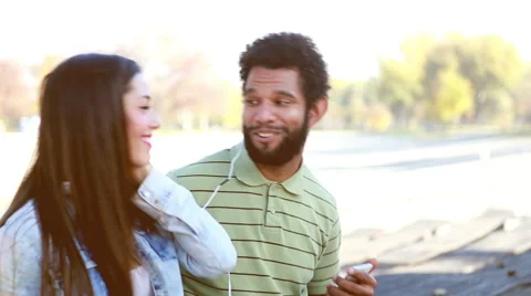 Happy couple with shared earphones listening to music at park Stock Footage 59555090