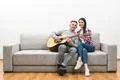 The happy couple sit on a sofa and play the guitar on the white wall backgrou Photo