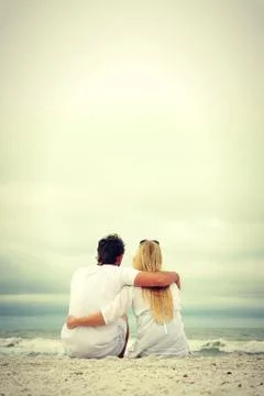 Happy couple sitting on beach looking at ocean Stock Photos