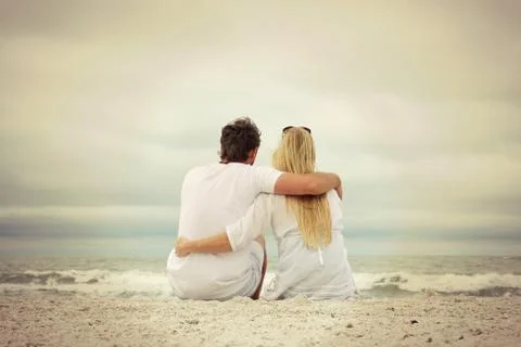 Happy couple sitting on beach looking at ocean Stock Photos