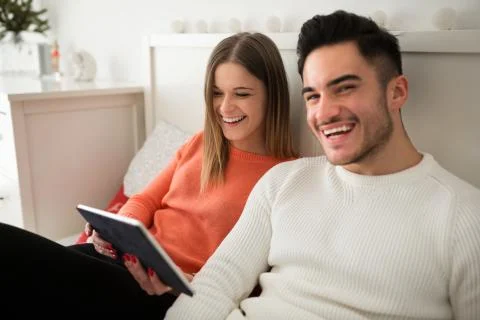 Happy couple sitting on bed using tablet Stock Photos