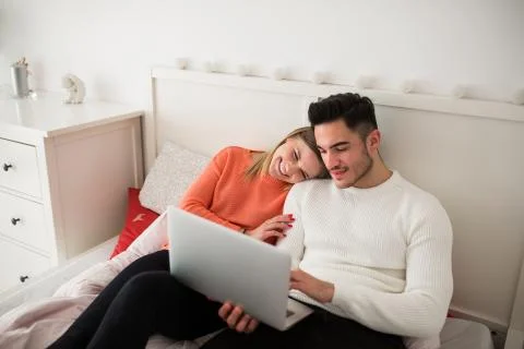 Happy couple sitting on bed using laptop Stock Photos