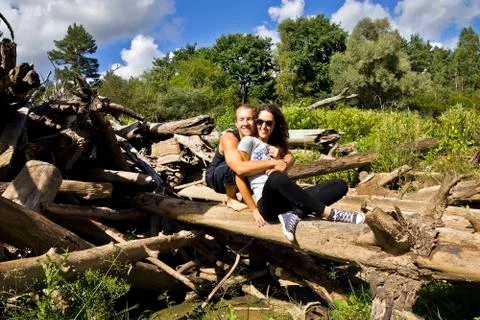 Happy couple sitting on the big log and enjoying the sunny day. Stock Photos