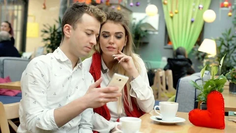 Happy couple sitting in the cafe on a date at Valentine's Day and looking on sma Stock-Footage 71870014