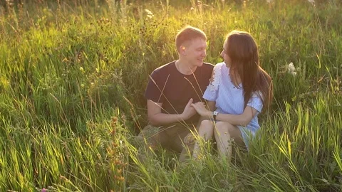 Happy couple sitting in a field and watching the sunset Stock Footage