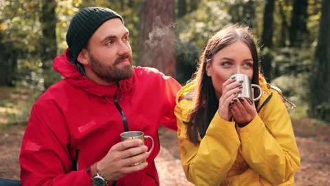 Happy couple sitting in forest, hugging and drinking hot tea from travel cups Stock Footage 147071086