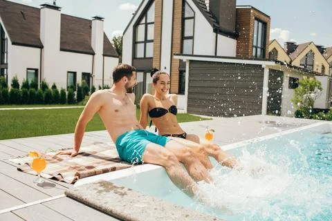 Happy couple sitting by the poolside in the backyard of their house. Man an.. Foto stock