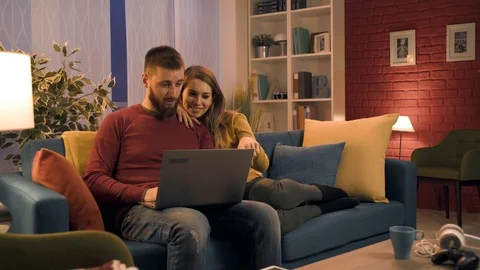 Happy couple sitting on the sofa and connecting with their laptop Stock Footage 128727675