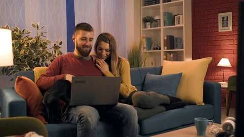 Happy couple sitting on the sofa and connecting with their laptop Stock Footage 128727730