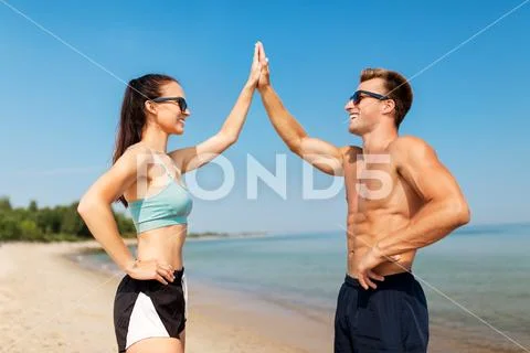 Happy couple in sports clothes and shades on beach Stock Photos