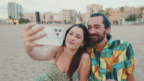 Happy couple taking selfie on mobile phone while sitting on the beach Stock Footage 227142989