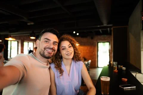 Happy couple taking selfie while drinking beer at the bar counter Stock Photos