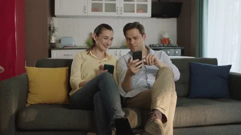 Happy couple talking laughing on sofa looking at smartphone using apps. Stock Footage 190633751