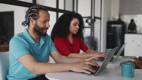 Happy couple in their 20s working on laptops and discussing online project Stock Footage 332803712