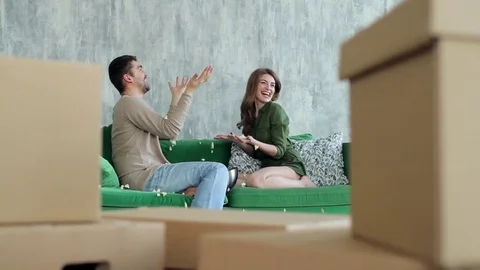 Happy Couple Throwing Popcorn Sitting on Sofa Among Boxes Moving Video stock 76023533
