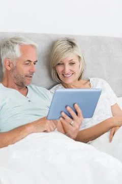Happy couple using digital tablet in bed Stock Photos