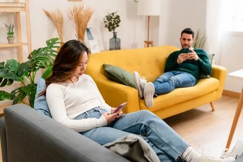 Happy couple using smartphone on sofa Stock Photos