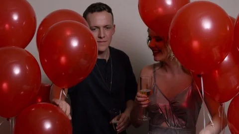 Happy Couple Walks Through Red Balloons While Holding Champagne Glasses Stock Footage 84807987