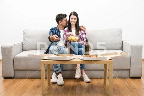 The happy couple watching tv with a pizza and a beer on the white background Stock Photos