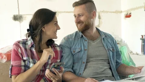 Happy couple with working with smartphone and documents sitting on floor at new  Vídeo Stock 80497553