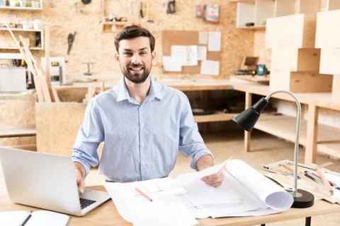 Happy craftsman entering data from page to gadget at workshop Stock Photos