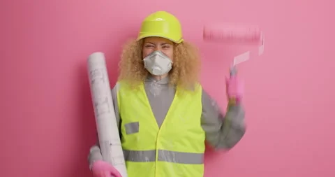 Happy curly haired construction worker makes yes gesture holds painting roller Stock Footage 155490151
