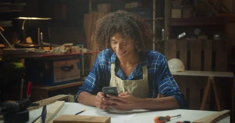 Happy curly joiner master using smartphone online chatting in social media in Stock Footage 140448656