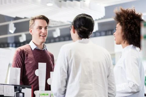 Happy customer talking with two helpful pharmacists in a contemp 스톡 사진