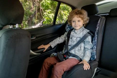 Happy cute boy of elementary age in denim jacket and brown pants sitting in car Stock Photos