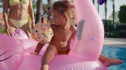 Happy cute boy is sitting on inflatable flamingo with mother in swimming pool Stock Footage 244346216