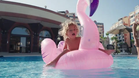 Happy cute boy is sitting on inflatable flamingo with mother in swimming pool Stock Footage 244346229