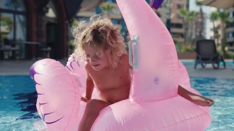 Happy cute boy is sitting on inflatable flamingo with mother in swimming pool Stock Footage 244346243