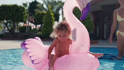 Happy cute boy is sitting on inflatable flamingo with mother in swimming pool Stock Footage 244346255