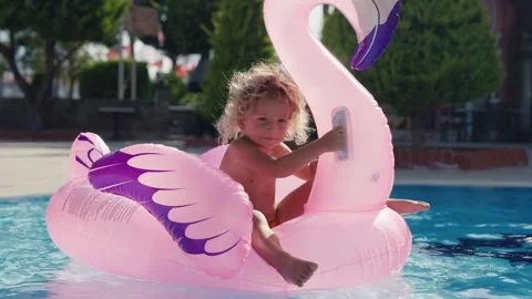 Happy cute boy is sitting on inflatable flamingo with mother in swimming pool Stock Footage 244467181