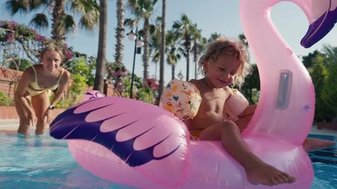 Happy cute boy is sitting on inflatable flamingo with mother in swimming pool Stock Footage 244467256